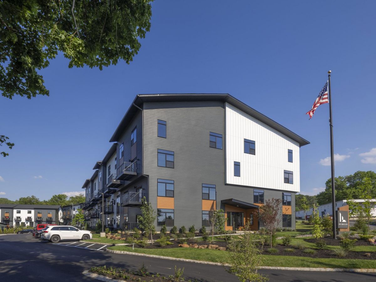 Westrum Corporate Modern three-story apartment building with parked cars, landscaped grounds, and an American flag on a sunny day.
