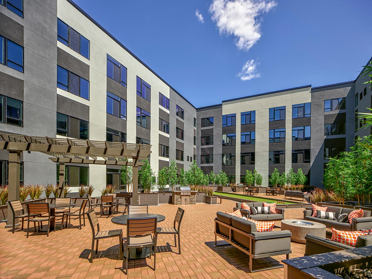 Westrum Corporate Modern apartment courtyard at Luxor Bala Cynwyd with patio furniture, fire pit, and greenery on a sunny day with blue sky.