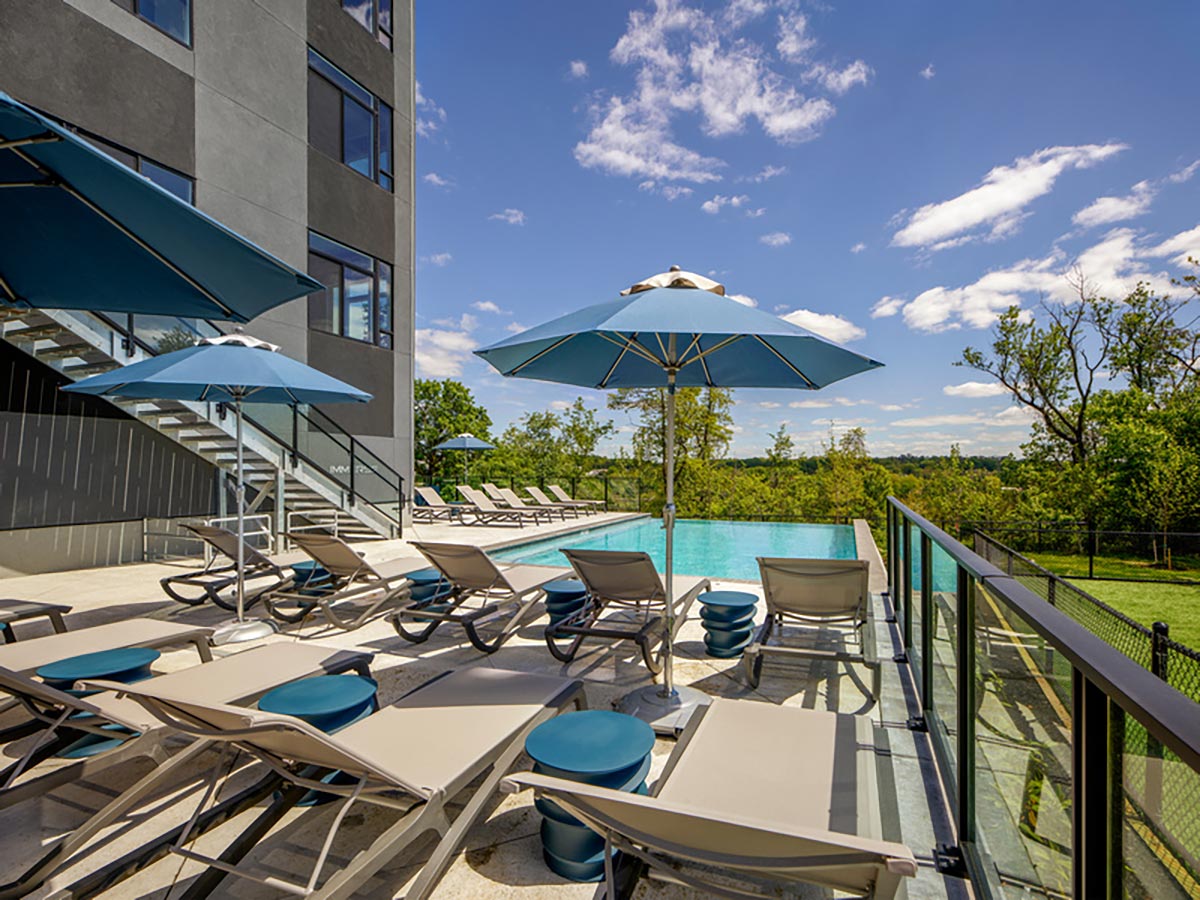 Westrum Corporate Lounge chairs and blue umbrellas await by the outdoor pool at Luxor luxury apartments in Bala Cynwyd on a sunny day.