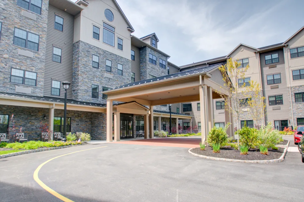 Westrum Corporate Pinnacle at Plymouth Meeting: a four-story building with stone and beige siding, covered entrance, driveway, and landscaped greenery.