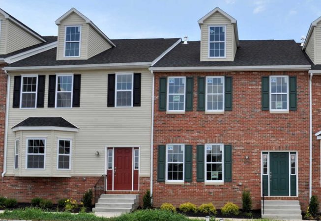Westrum Corporate Two-story brick and siding townhouses with green and red doors, dormer windows, and small front gardens.