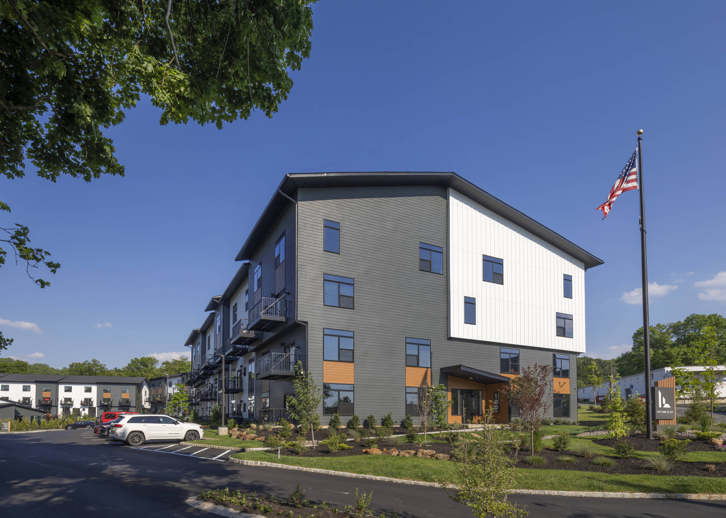 Westrum Corporate Foundry Flats is a modern three-story apartment building with cars parked outside, landscaped grounds, and an American flag on a sunny day.
