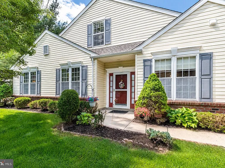 Westrum Corporate Charming single-story home in Hatfield Township with yellow siding, gray shutters, red doors, and landscaped garden beds lining the walkway.