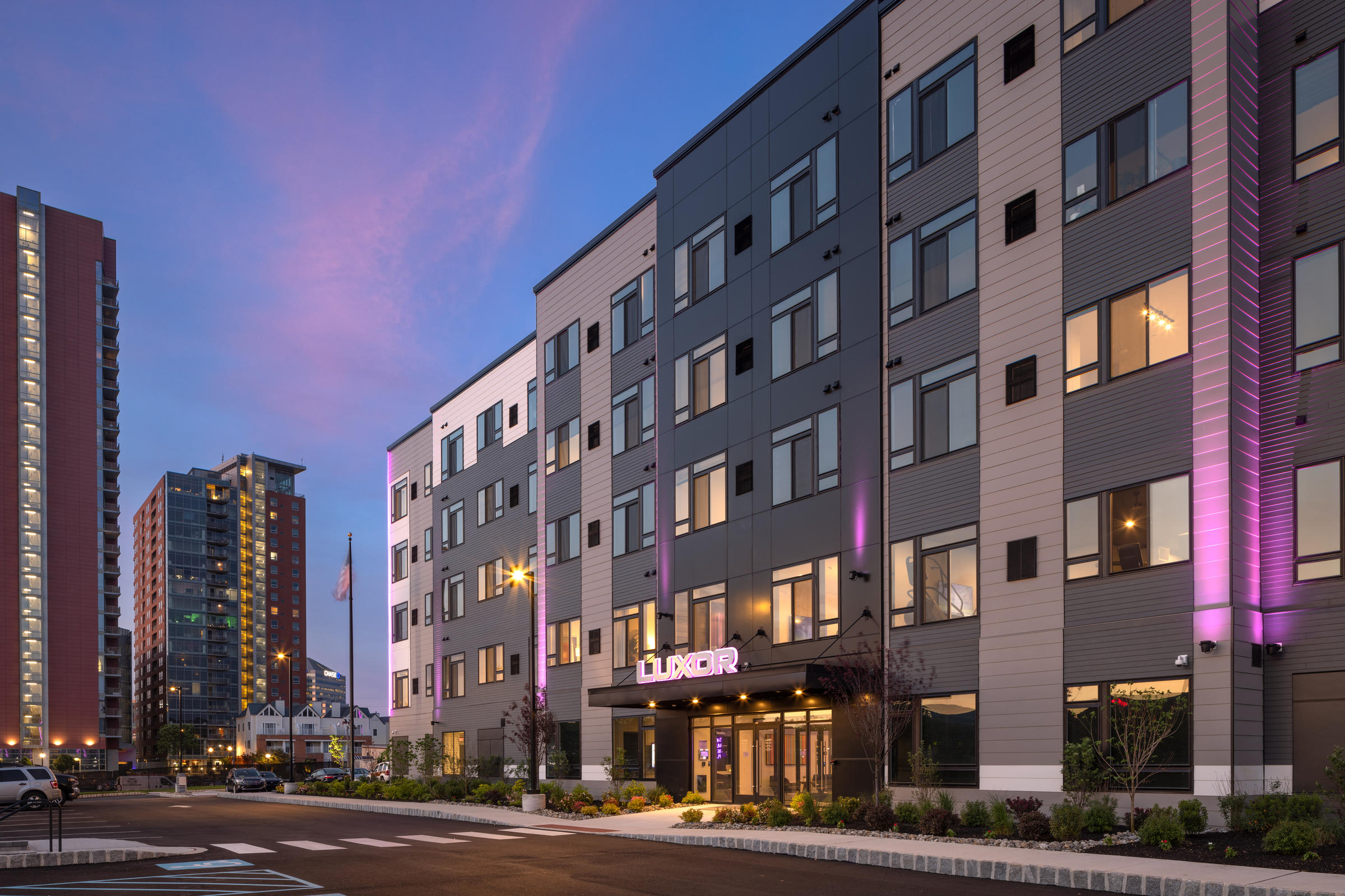 Westrum Corporate Modern apartment building with the sign "LUXOR MONTGOMERYVILLE" lit in purple, surrounded by city buildings at sunset.