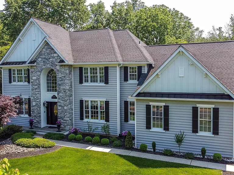 Westrum Corporate Two-story gray house with stone accent in Lower Gwynedd Township, black shutters, manicured lawn, and shrubs surrounded by trees.
