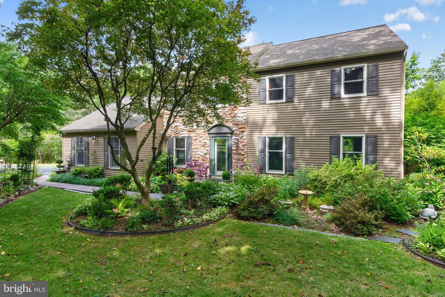 Westrum Corporate Two-story house in Lower Providence Township with stone and siding exterior, black shutters, lush lawn, trees, and garden.