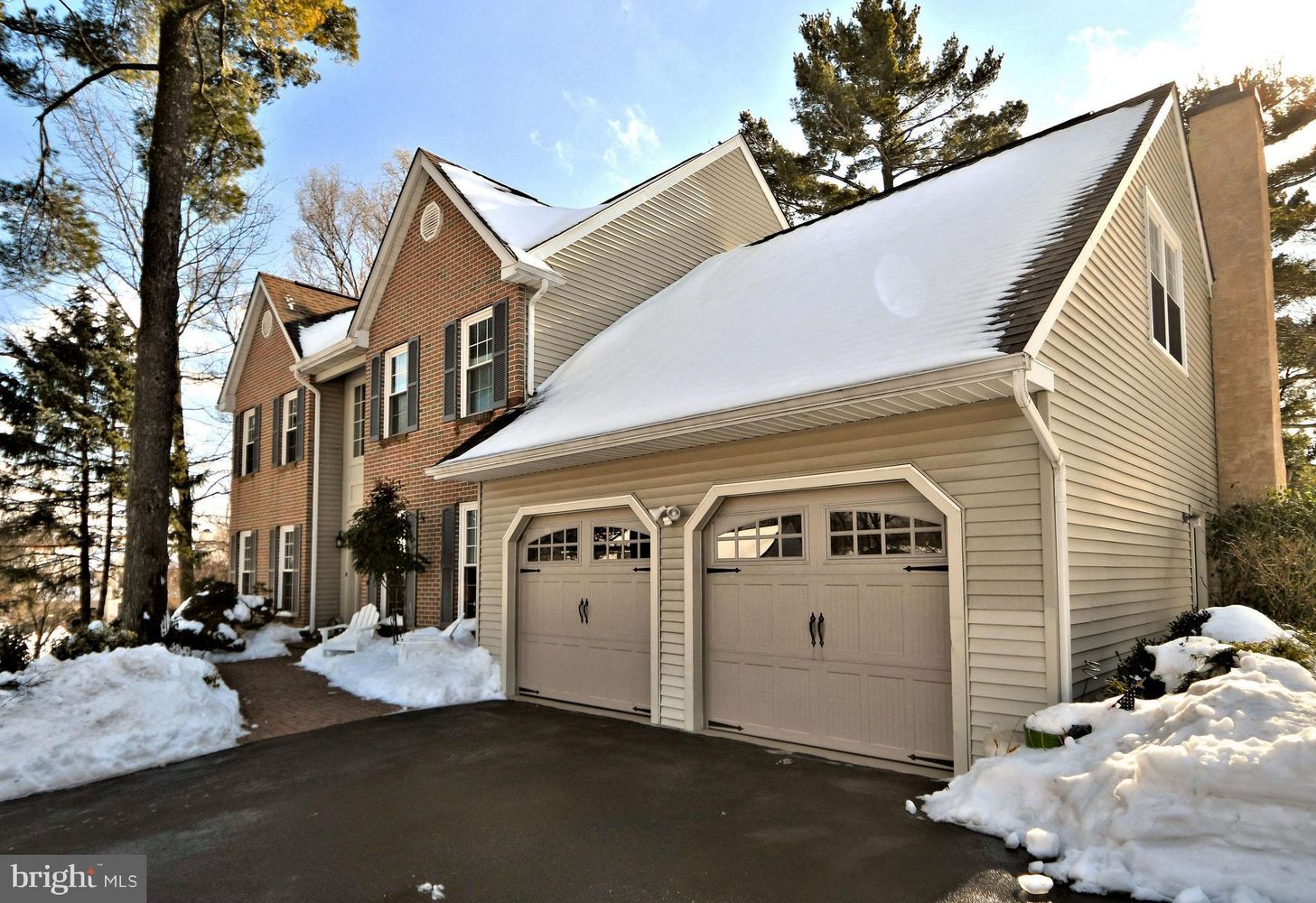 Westrum Corporate Charming two-story Montgomery Township home with brick and siding, snowy roof, double garage, and a driveway dusted in snow.