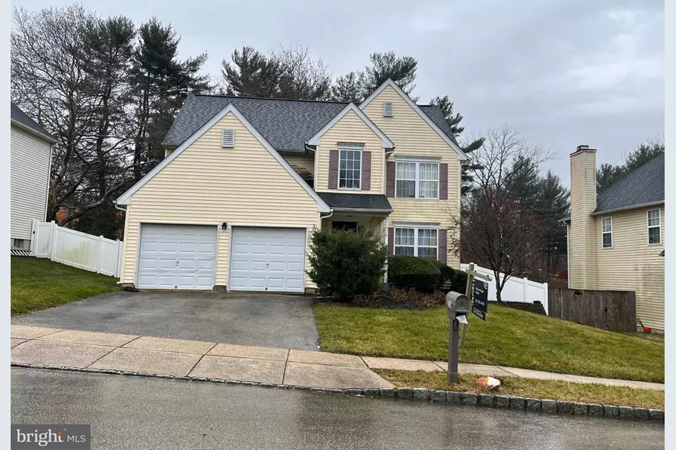 Westrum Corporate Two-story beige house with white trim, double garage, sloped driveway, and a green lawn on a cloudy day.