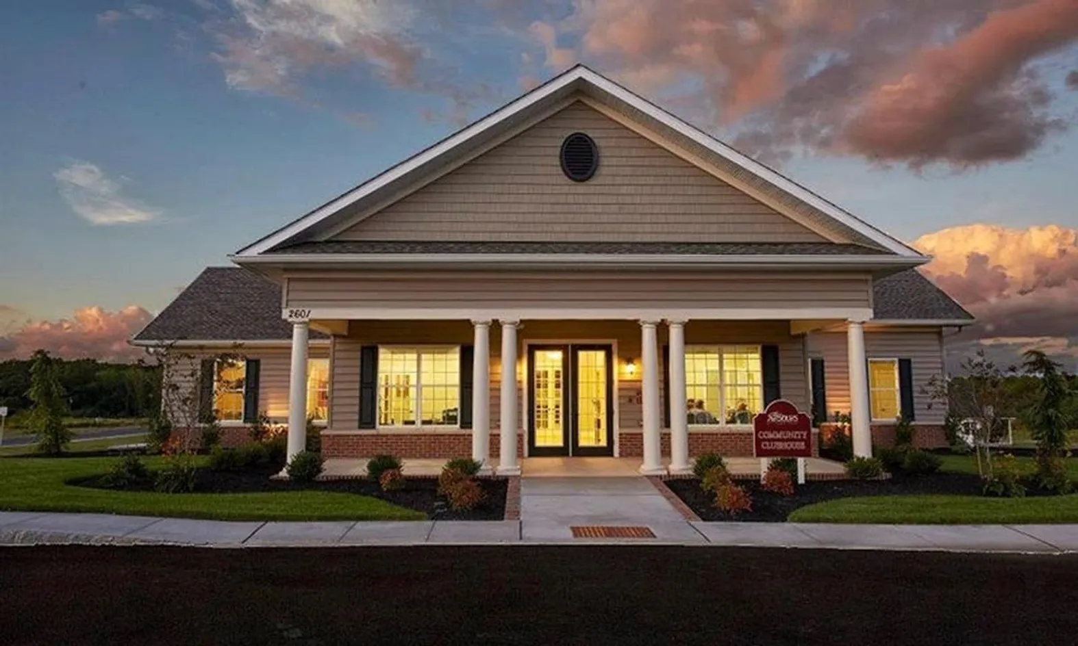 Westrum Corporate Single-story building with columns, lit warmly from inside, at dusk with a sign reading “Community Clubhouse” on the lawn.
