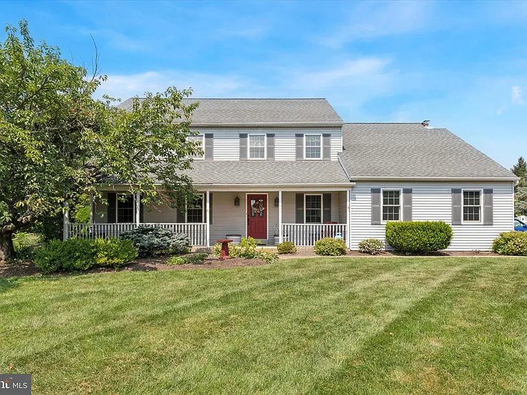 Westrum Corporate Two-story house with gray siding in Towamencin Township, red door, large lawn, green bushes, and bright blue sky in Montgomery County.