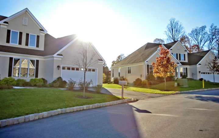 Westrum Corporate Suburban street in Whitemarsh Township with modern houses, green lawns, shady trees, and a bright sun in the background.