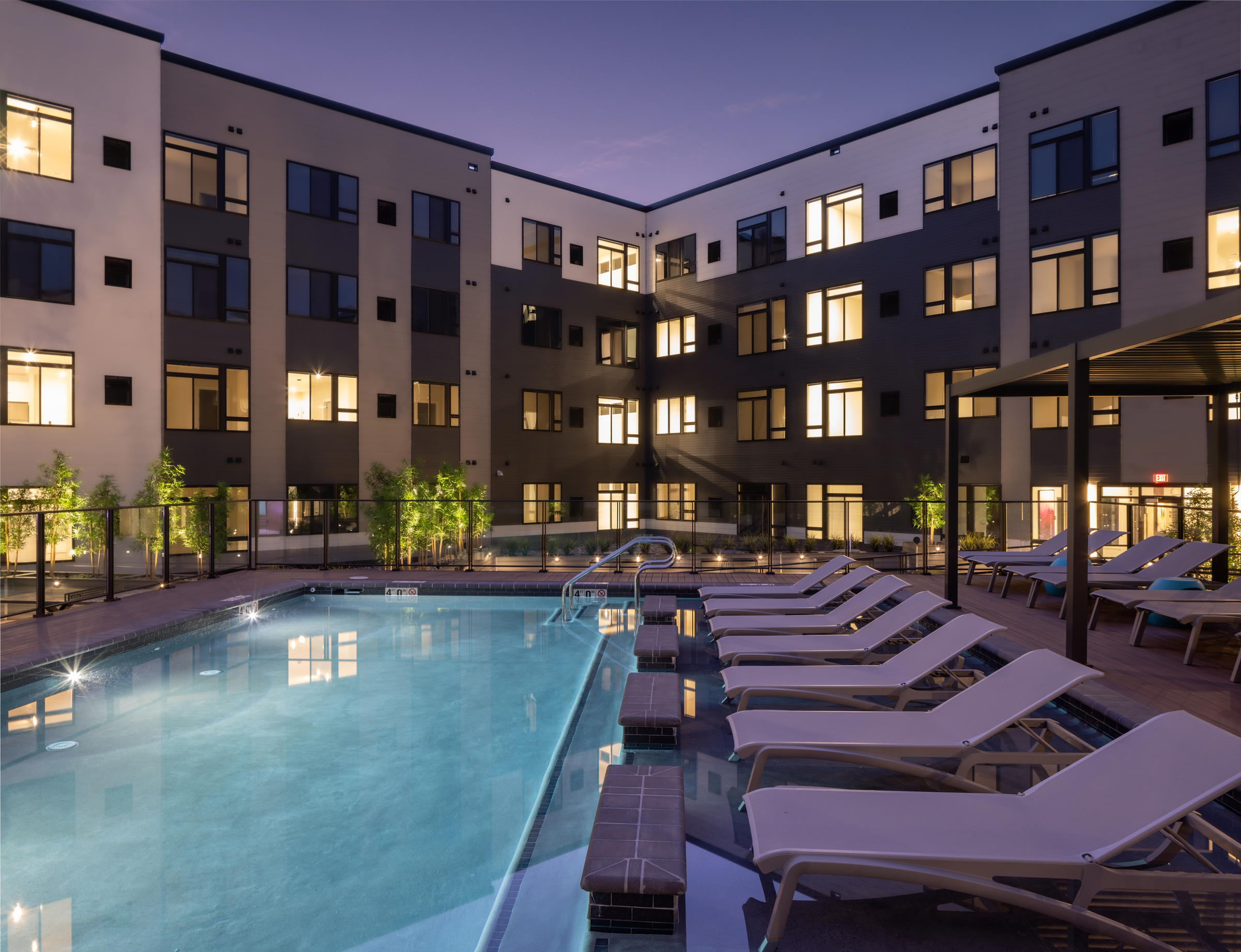 Westrum Corporate Modern apartment building with lit windows surrounds a pool with lounge chairs at dusk.