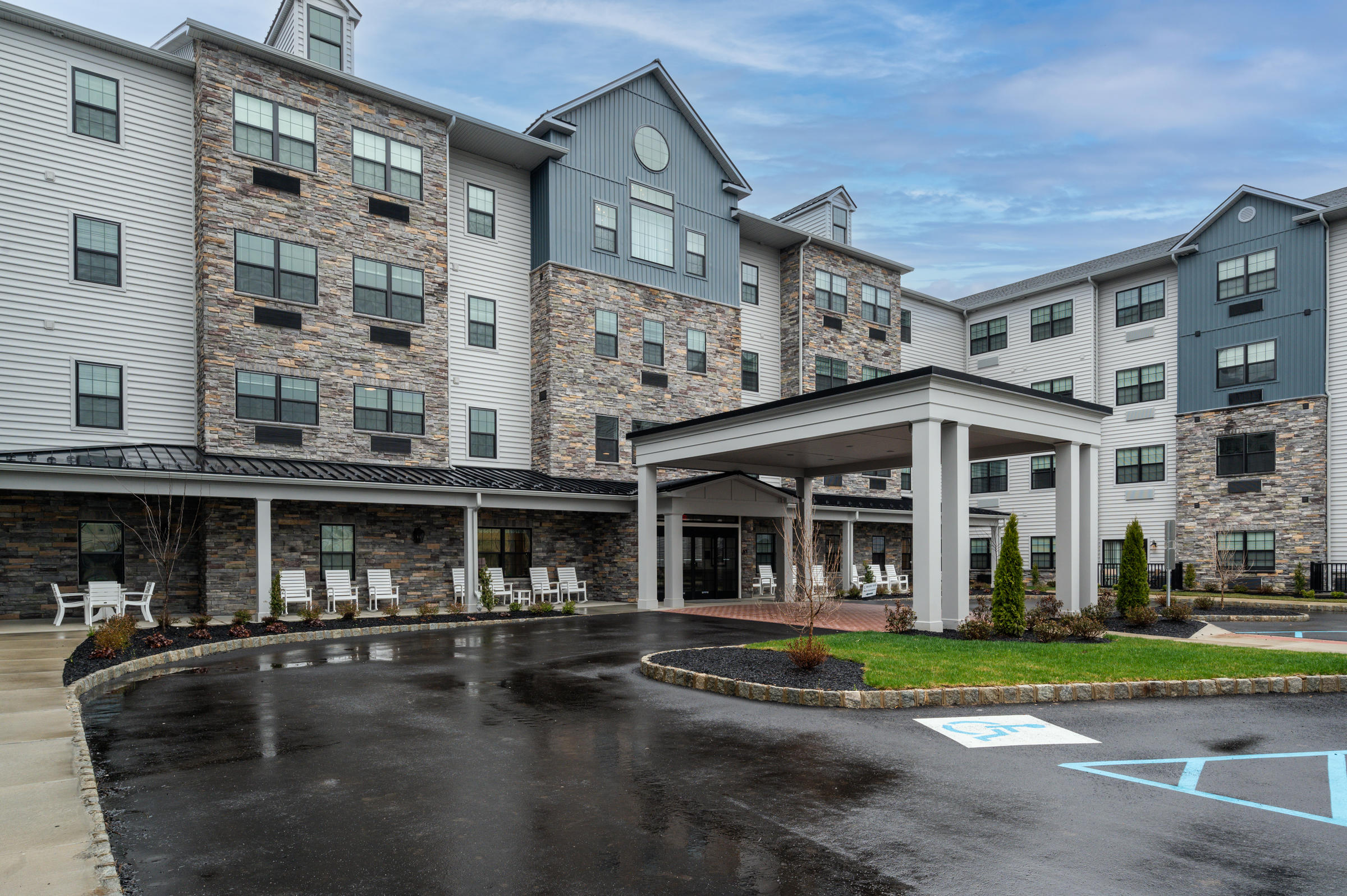 Westrum Corporate Four-story modern building with stone facade, covered entrance, rocking chairs, and wet pavement on a cloudy day.