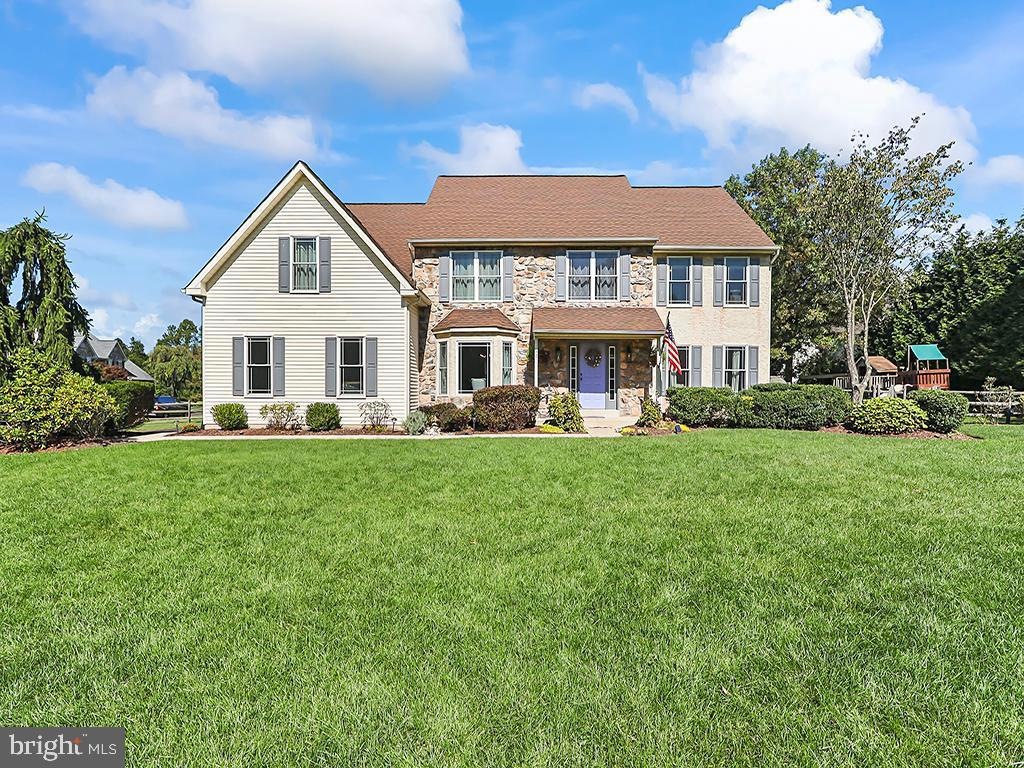 Westrum Corporate Charming two-story Buckingham Place home with stone and siding, lush green lawn, shrubs, and a bright sky dotted with clouds.
