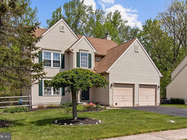 Westrum Corporate Two-story beige house in Buckingham Square with green shutters, double garage, manicured lawn, and a small tree in the sunny front yard.