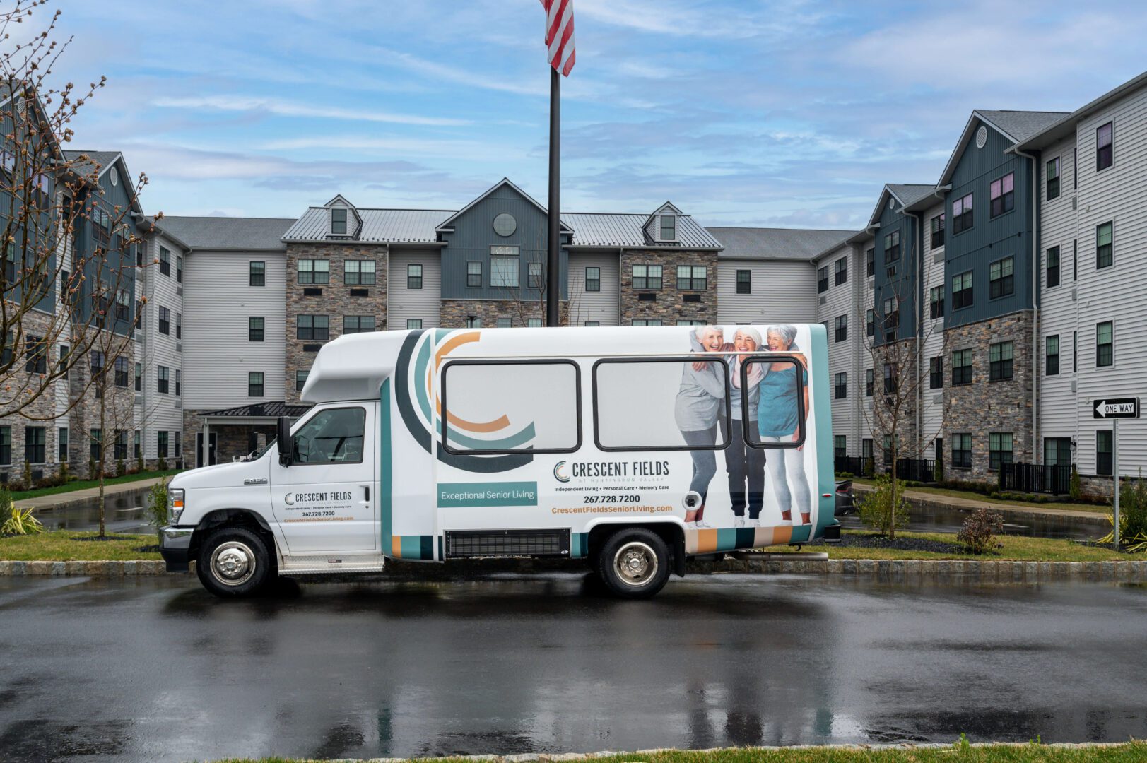 Westrum Corporate A white Crescent Fields van is parked in front of a large apartment building on a wet street, with an American flag in the background.