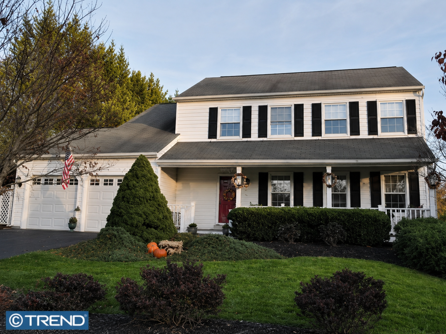 Westrum Corporate Two-story Highland Park suburban house with black shutters, front porch, and a well-kept lawn with bushes and pumpkins by the entrance.