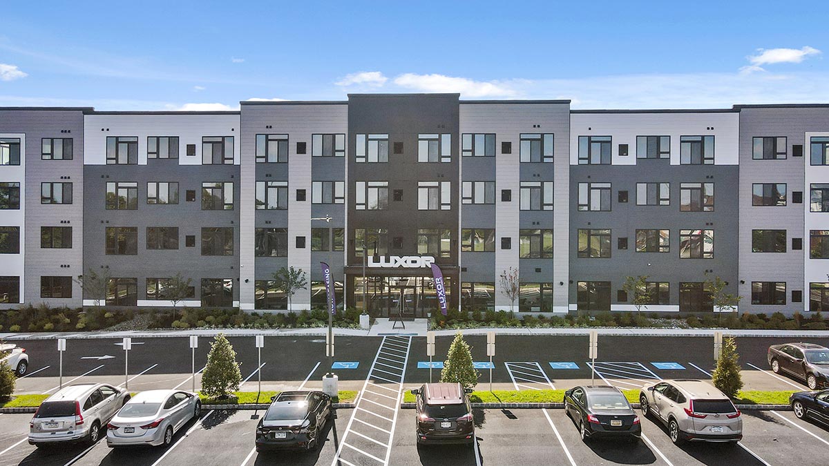Westrum Corporate A modern four-story apartment building with parked cars, visible “LUXOR” sign, and accessible parking spaces in front.