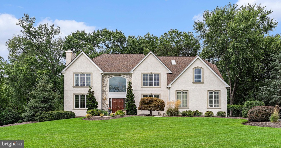 Westrum Corporate Two-story beige house with a brown roof, large windows, double front doors, and landscaped green lawn with bushes and trees.