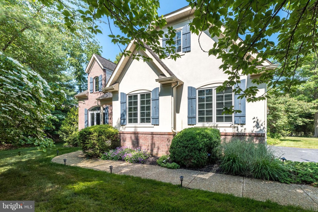 Westrum Corporate Gentry Manor: Two-story house with brick and stucco, large windows, shutters, garden, sidewalk, and trees basking in the sun.