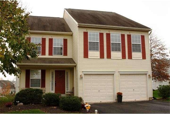 Westrum Corporate Charming two-story beige home in Perkiomen Greene with red shutters, double garage, red door, and bushes lining the front yard.