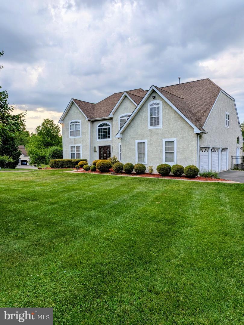 Westrum Corporate Two-story beige house with a brown roof, well-kept lawn, shrubs, and a three-car garage under a cloudy sky.