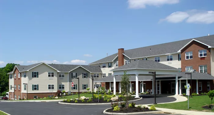 Westrum Corporate A large, modern senior living facility with a driveway, landscaped garden, and clear blue sky.