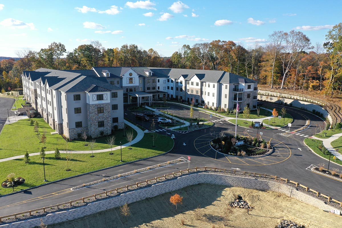Westrum Corporate Aerial view of a large, modern building with landscaped grounds, parking lot, and surrounded by trees under a blue sky.
