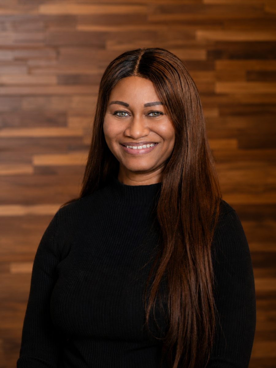 Westrum Corporate Smiling woman with long brown hair, wearing a black top, stands in front of a wooden wall. Shenika McCloud radiates confidence.