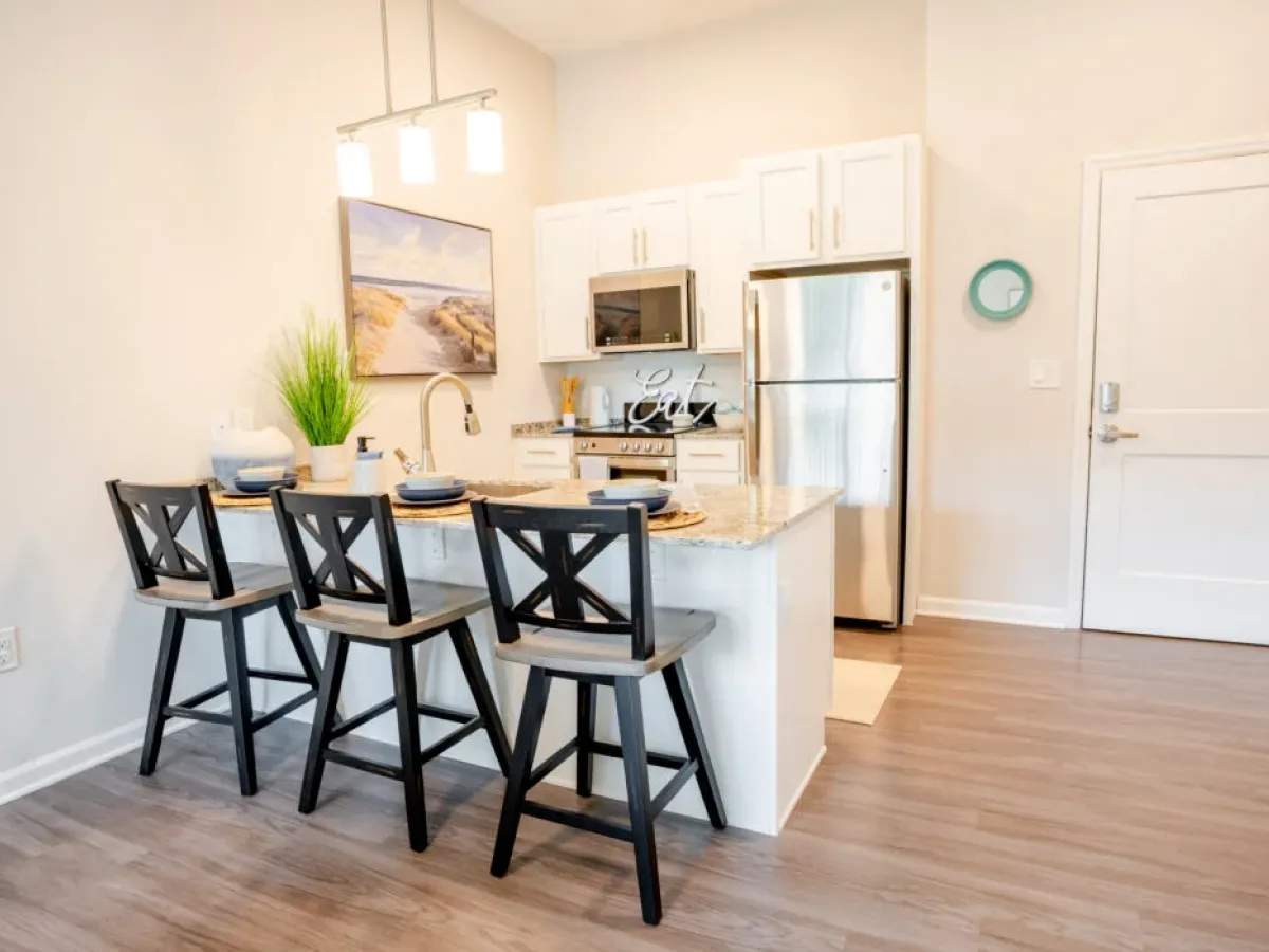 Westrum Corporate Modern Azalea kitchen with white cabinets, stainless appliances, and black barstools at a marble island set for dining in Cinnaminson.