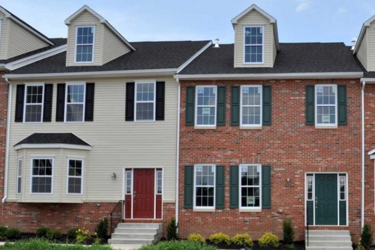 Westrum Corporate Two-story brick and siding townhouses with green and red doors, dormer windows, and small front gardens.
