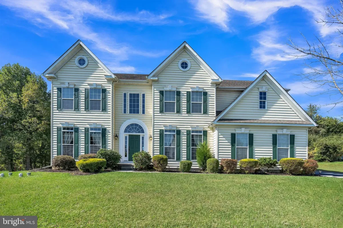 Westrum Corporate Two-story yellow house with green shutters, arched entry, and manicured lawn under a blue sky with scattered clouds.