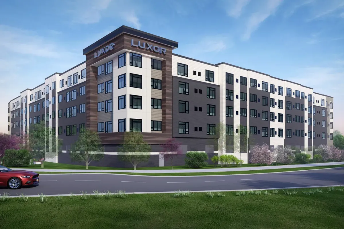 Westrum Corporate Modern five-story Luxor apartment in Fort Washington, featuring large windows, greenery, and a red car driving by out front.