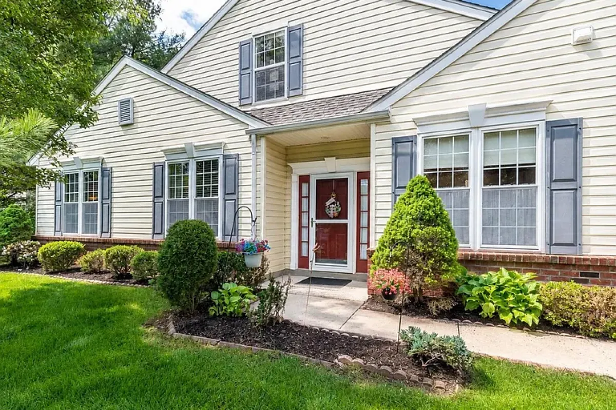 Westrum Corporate Charming single-story home in Hatfield Township with yellow siding, gray shutters, red doors, and landscaped garden beds lining the walkway.