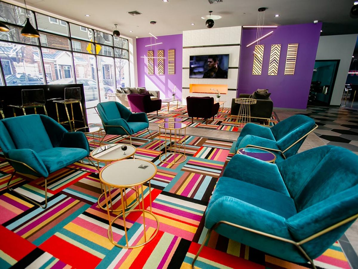 Westrum Corporate Colorful lounge at Hub at 31 Brewerytown features teal chairs, a striped rug, gold tables, TV on a purple wall, and large windows.
