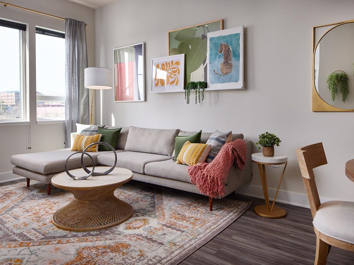 Westrum Corporate Modern living room at Luxor Wilmington with gray sectional, coffee table, wall art, large window, decorative rug, and plants.