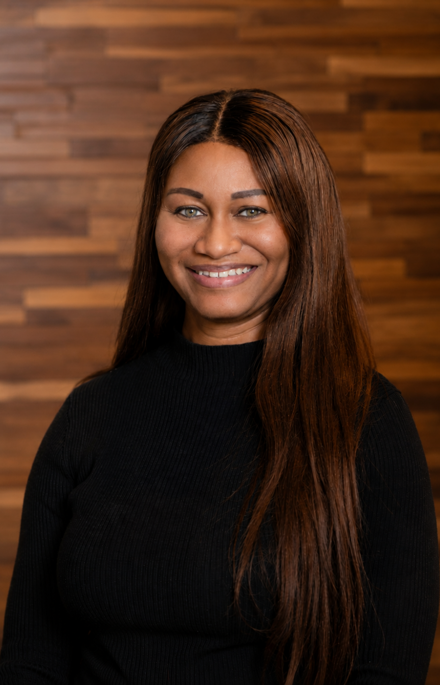 Westrum Corporate Smiling woman with long brown hair, wearing a black top, stands in front of a wooden wall. Shenika McCloud radiates confidence.