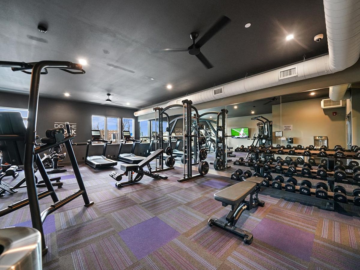 Westrum Corporate Modern gym at Luxor Lansdale with exercise machines, free weights, benches, mirrors, and purple carpet flooring.
