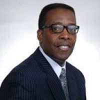 Westrum Corporate Darrell Clarke, wearing glasses and a dark striped suit with a patterned tie, smiles at the camera against a plain background.