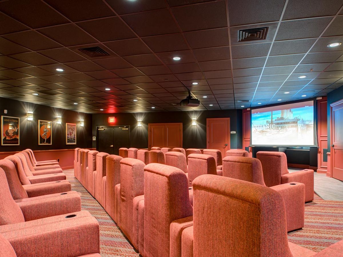 Westrum Corporate Rows of red theater seats face a large screen in Mercer Hill’s cozy home theater, perfect for senior living in Doylestown.