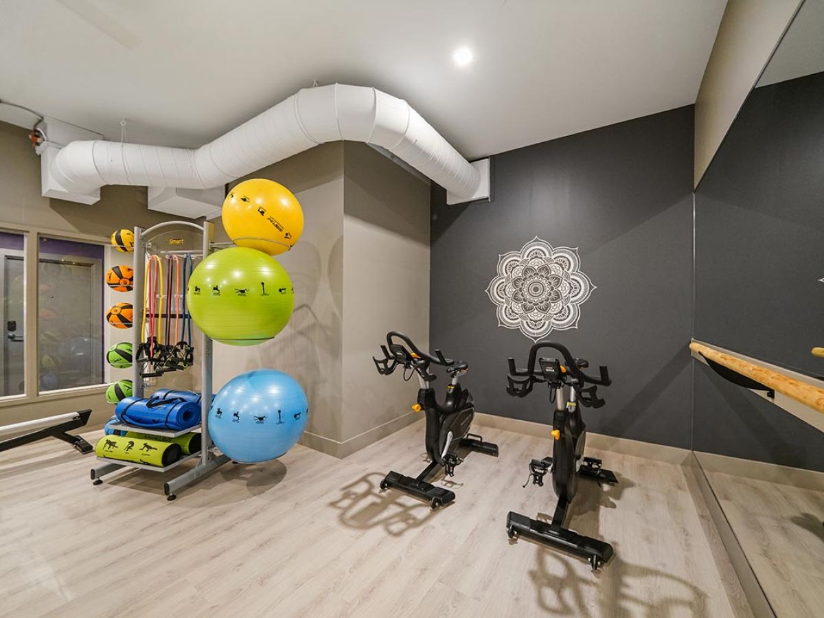 Westrum Corporate Modern Luxor Lansdale gym with exercise bikes, yoga balls, resistance bands, and mirrored wall featuring mandala designs on gray paint.