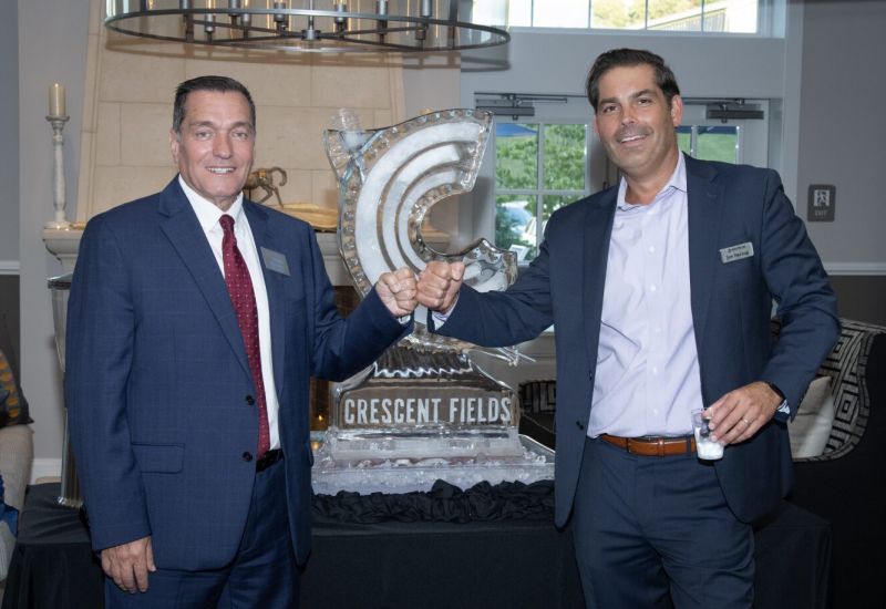 Westrum Corporate Two men in suits smile and fist bump in front of an ice sculpture that reads "Crescent Fields.