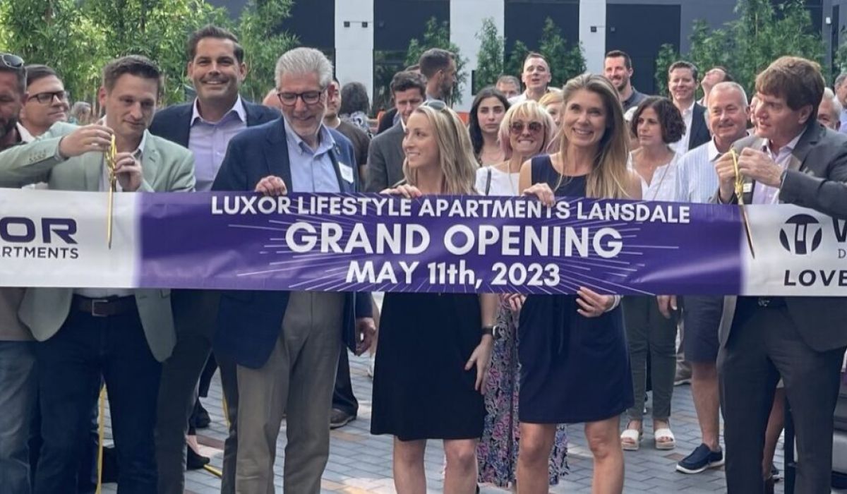 Westrum Corporate A group of people smile and pose with a "Grand Opening" banner for Luxor Lifestyle Apartments, May 11th, 2023.