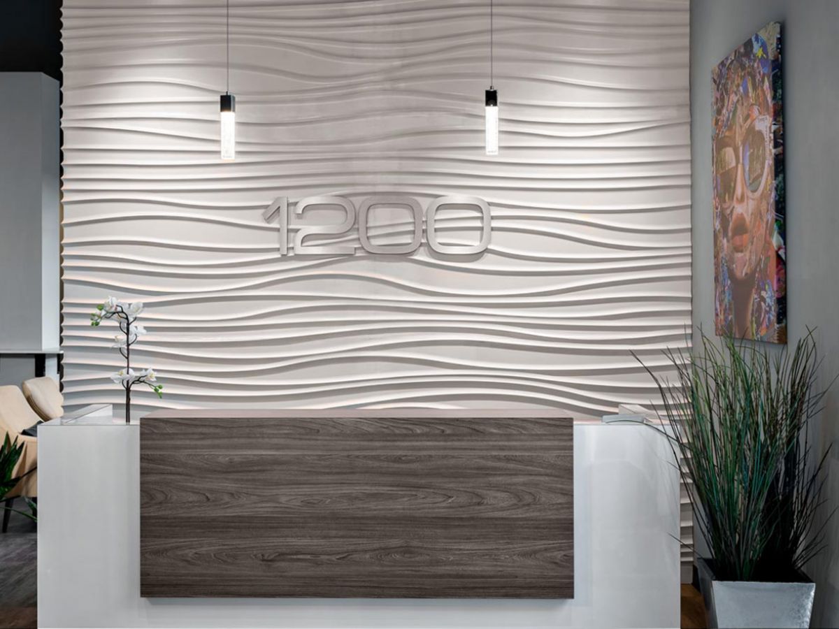 Westrum Corporate Modern reception area at 1200 Washington apartments features a wood desk, wavy wall panel, plants, and vibrant wall art.