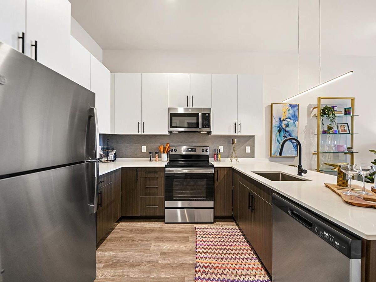 Westrum Corporate Modern Luxor Lansdale kitchen with stainless steel appliances, white and dark cabinets, and a patterned rug on a wood floor.