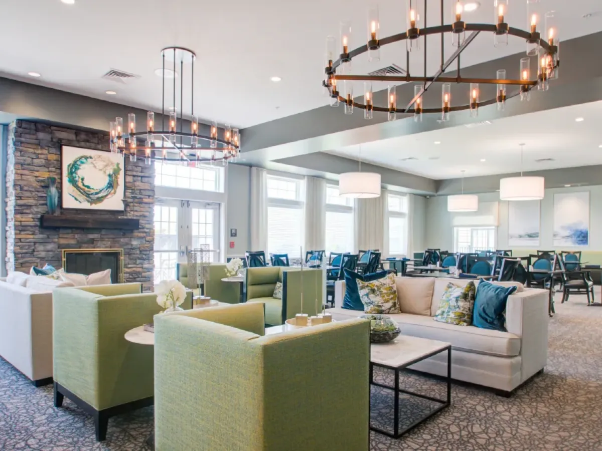 Westrum Corporate Modern lounge at Pinnacle, Plymouth Meeting: green sofas, white chairs, chandeliers, big windows, and art above a stone fireplace.