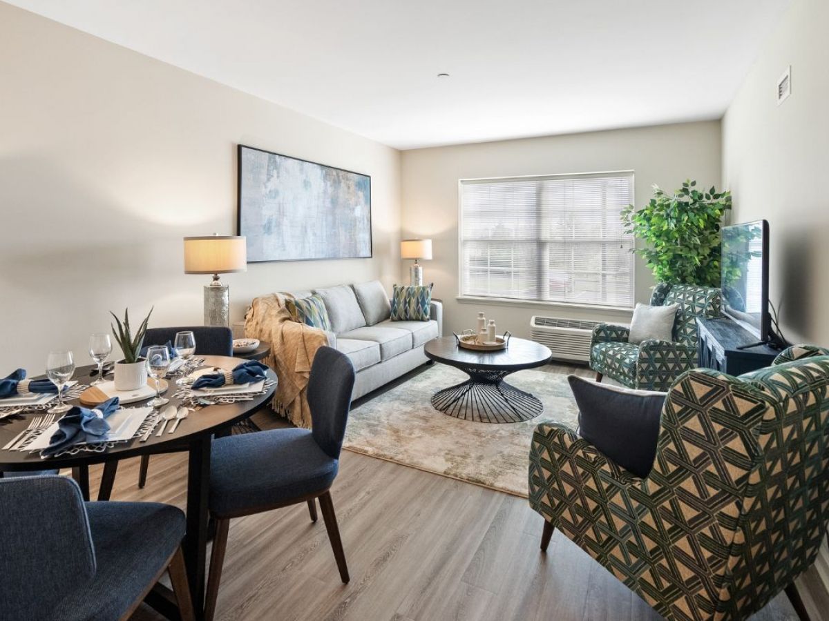 Westrum Corporate Modern living room at Arbour Square in Harleysville, ideal for senior living, with sofa, dining set, large window, TV, and potted plant.