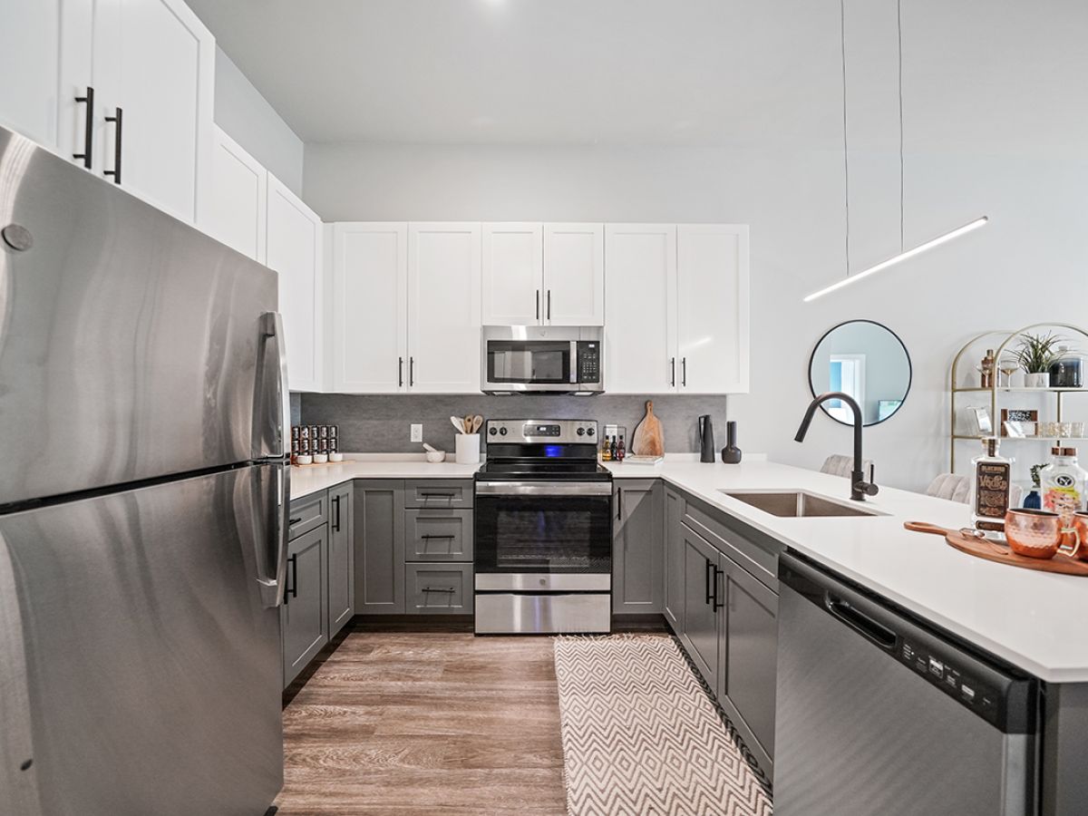 Westrum Corporate Modern kitchen at Luxor Phoenixville with stainless steel appliances, gray cabinets, and a round mirror above sleek open shelves.