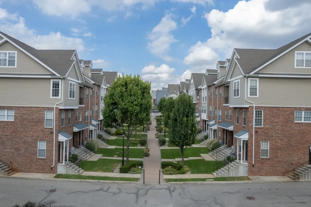 Westrum Corporate Row of townhouses with brick and tan siding, landscaped yards, trees, and a central walkway under a partly cloudy sky.