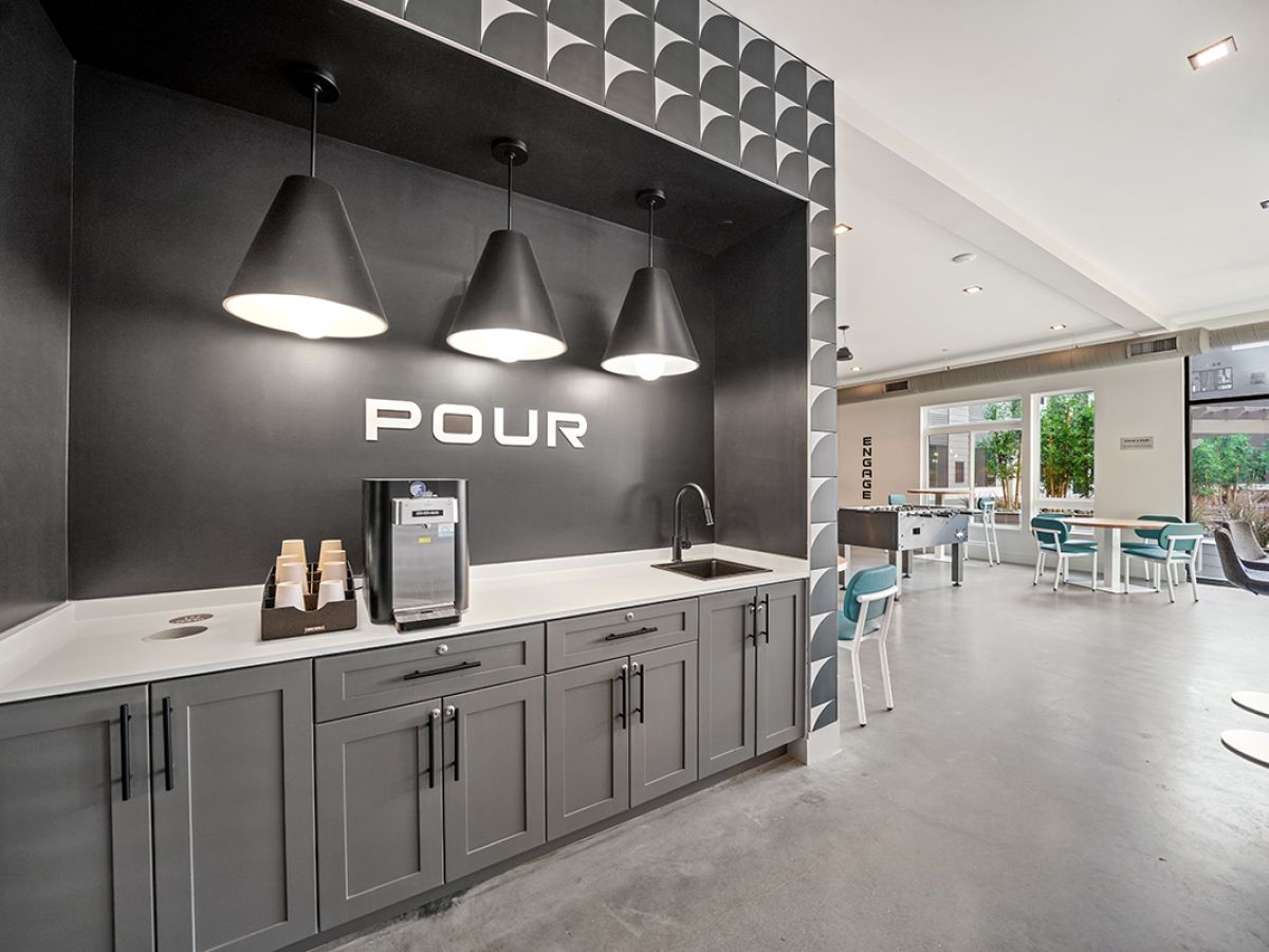 Westrum Corporate Modern Luxor coffee station with a large “POUR” sign, cups, and seating in a bright Phoenixville lounge space.
